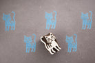 Bright tail cat wooden block printing stamp creating light blue cat prints on textured grey paper background.