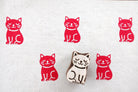 Meditative cat wooden block printing stamp creating bold red cat prints on white fabric background.
