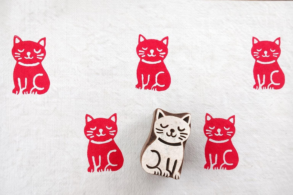Meditative cat wooden block printing stamp creating bold red cat prints on white fabric background.