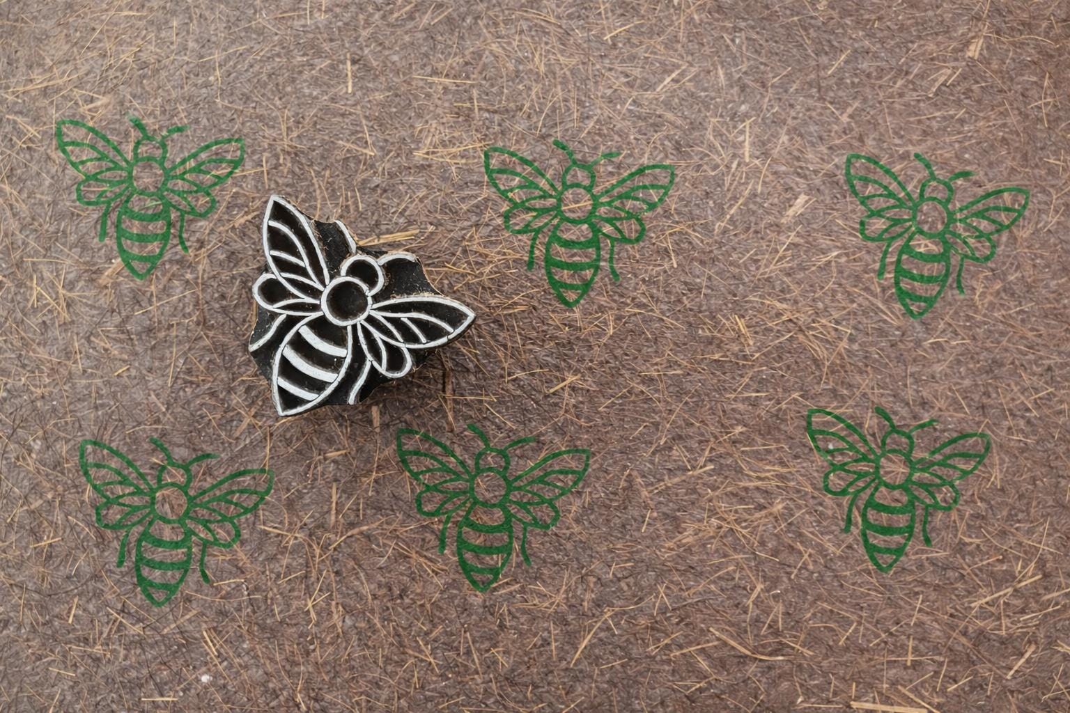 Bee wooden block printing stamp creating green bee prints on textured handmade paper.
