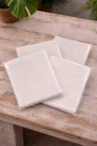 Pack of five handmade off-white deckle edge paper sheets wrapped in clear plastic, showing natural cream paper tone on a wooden surface