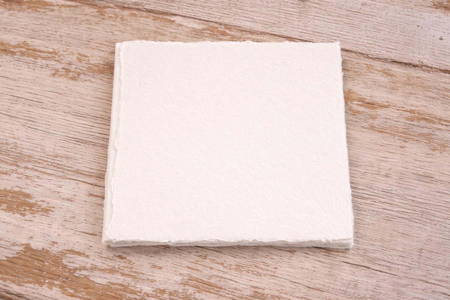 Pack of five handmade off-white deckle edge paper sheets, showing natural cream paper tone on a wooden surface