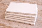 Single off-white handmade paper sheet with deckle edges laid flat on a wooden table, showing soft cream color and textured surface