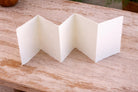 Accordion folded handmade paper in off-white cream color showing multiple panels and soft deckle edges on a wooden surface