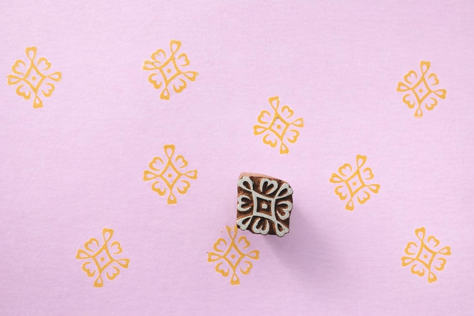 Indian wooden printing stamp creating repeating yellow textile pattern on pastel paper