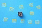 Spiral geometric wooden block stamp creating repeating pattern on blue sheet