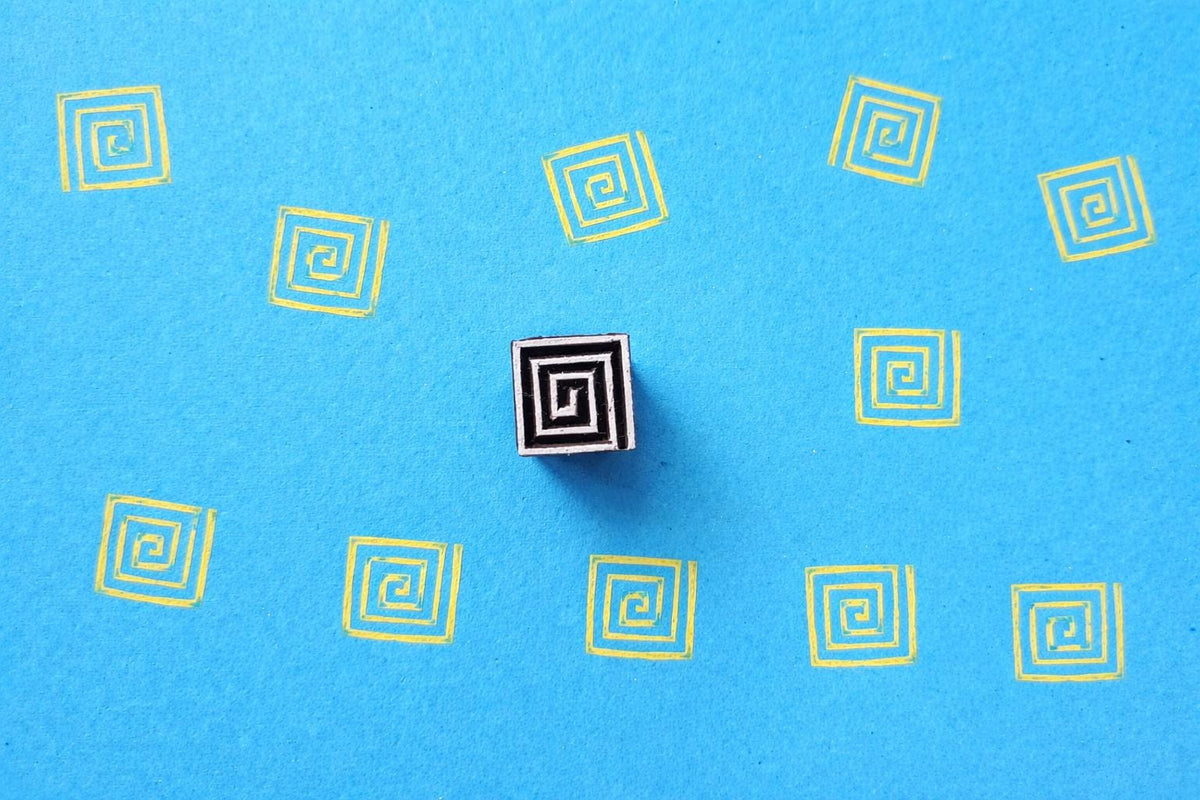 Spiral geometric wooden block stamp creating repeating pattern on blue sheet