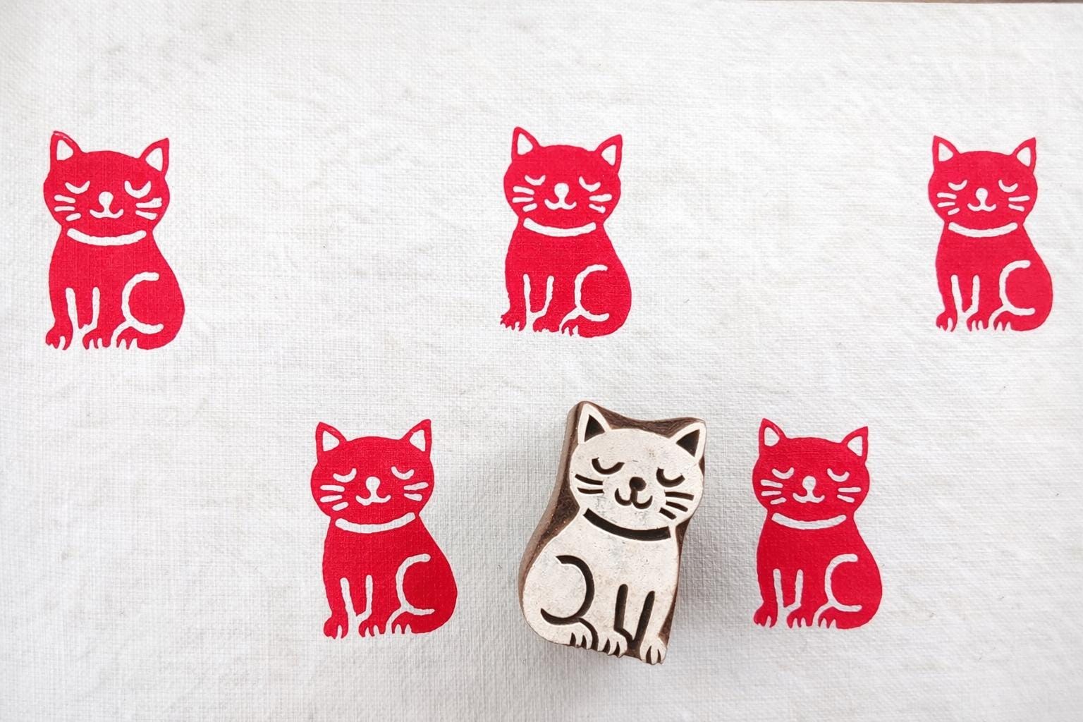 Meditative cat wooden block printing stamp creating bold red cat prints on white fabric background.