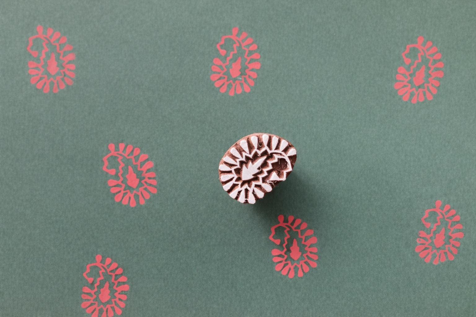 Paisley bloom wooden block printing stamp creating red prints on green handmade paper.