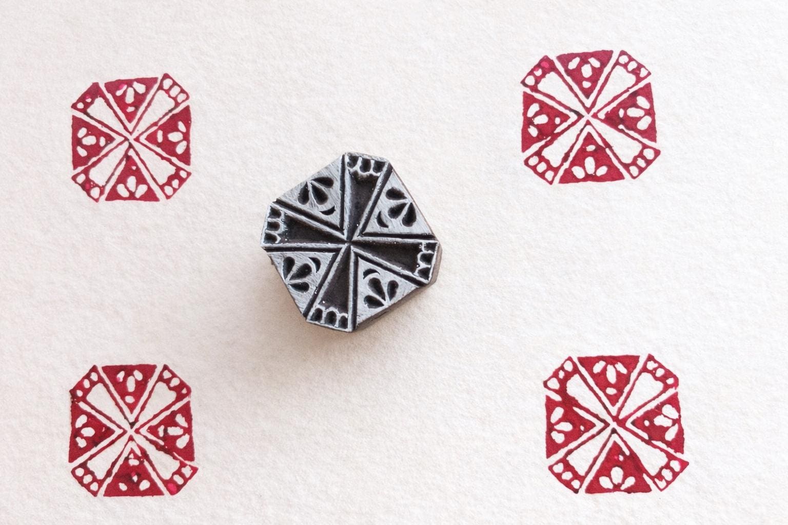 Hand carved wooden stamp creating red circular radial pattern on fabric
