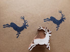 Hand-carved wooden deer block stamp with dark blue leaping stag prints on paper in a rustic woodland style