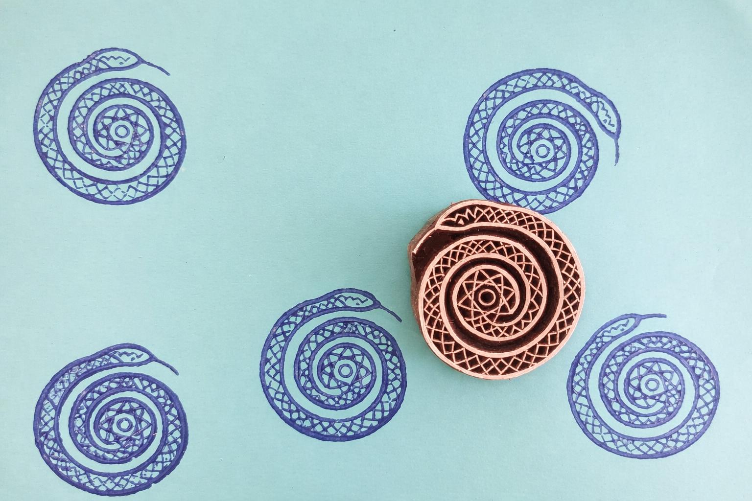 Hand-carved spiral snake stamp with blue geometric serpent prints on paper
