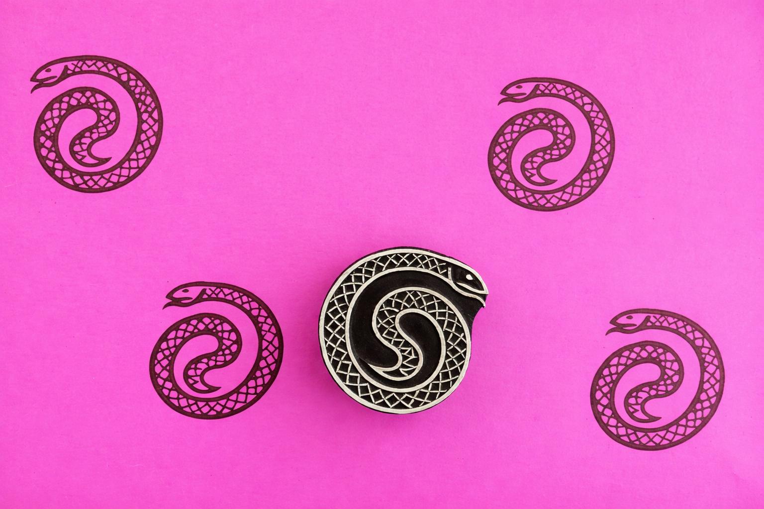 Coiled snake wood block stamp with black serpent prints on bright pink background