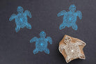 Hand carved turtle block printing stamp creating decorative pattern on dark paper