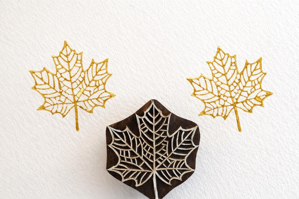 Crownleaf wooden stamp producing intricate gold maple leaf prints on white textured background