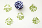 Hand carved wooden block stamp with seashell design creating repeating coastal pattern in green ink on paper
