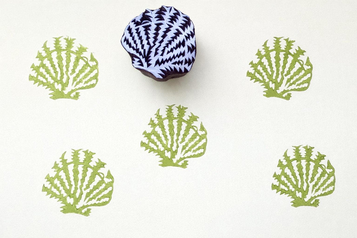 Hand carved wooden block stamp with seashell design creating repeating coastal pattern in green ink on paper