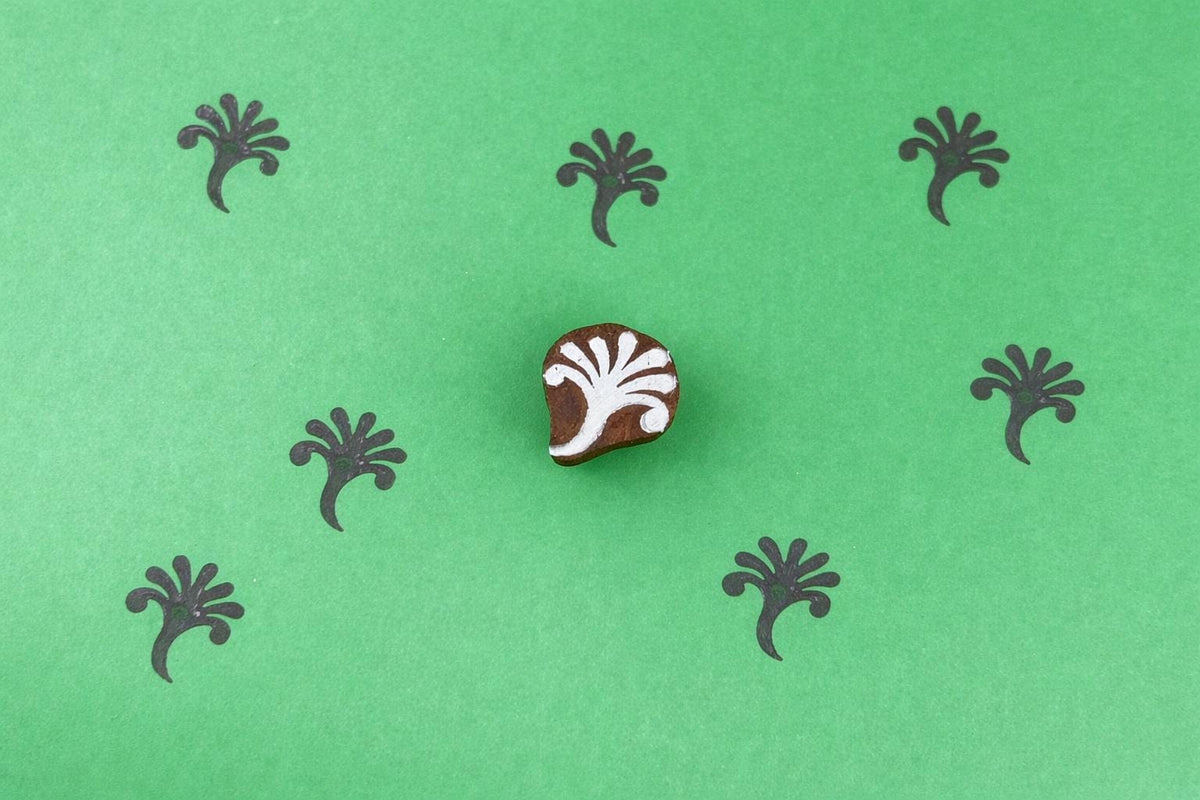 Small hand carved wooden block stamp with abstract botanical sprig design printed in repeating pattern on green background