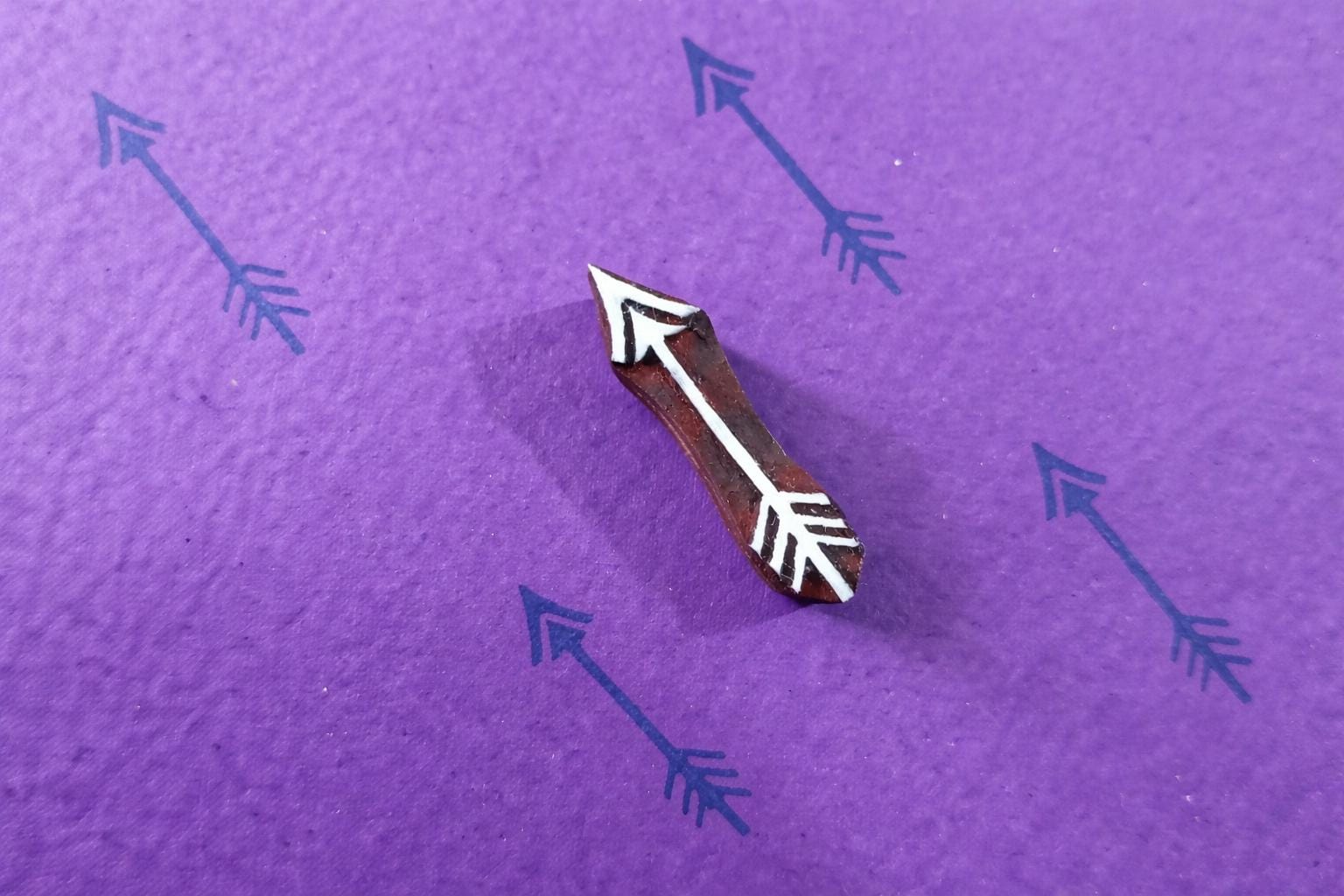 Single wooden arrow stamp creating a repeating minimalist arrow pattern on purple paper.