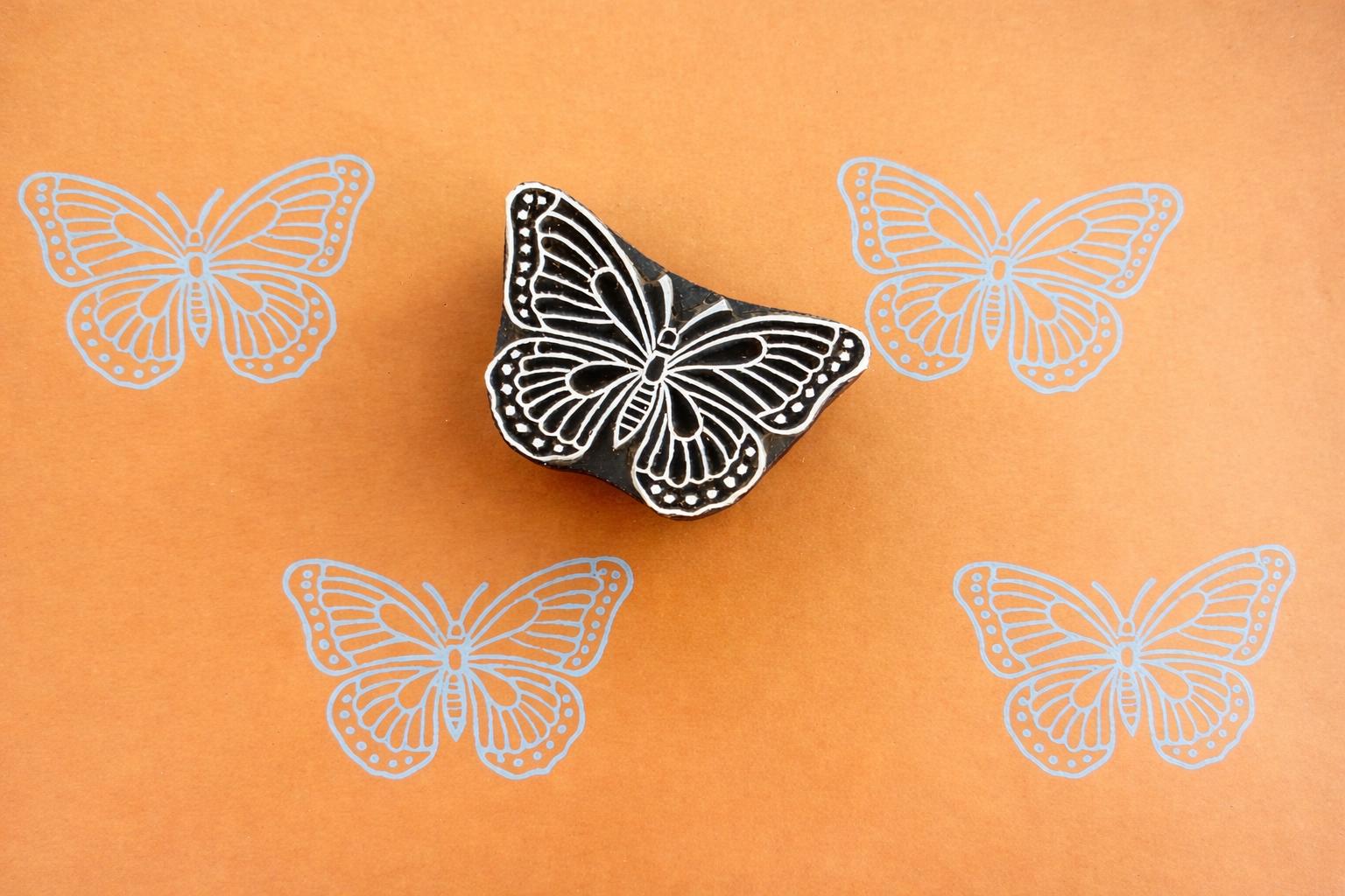 Wooden butterfly block stamp with pink butterfly prints on orange background