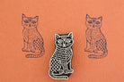 Hand carved wooden stamp of a patterned cat with textured body details printed in dark ink on orange paper