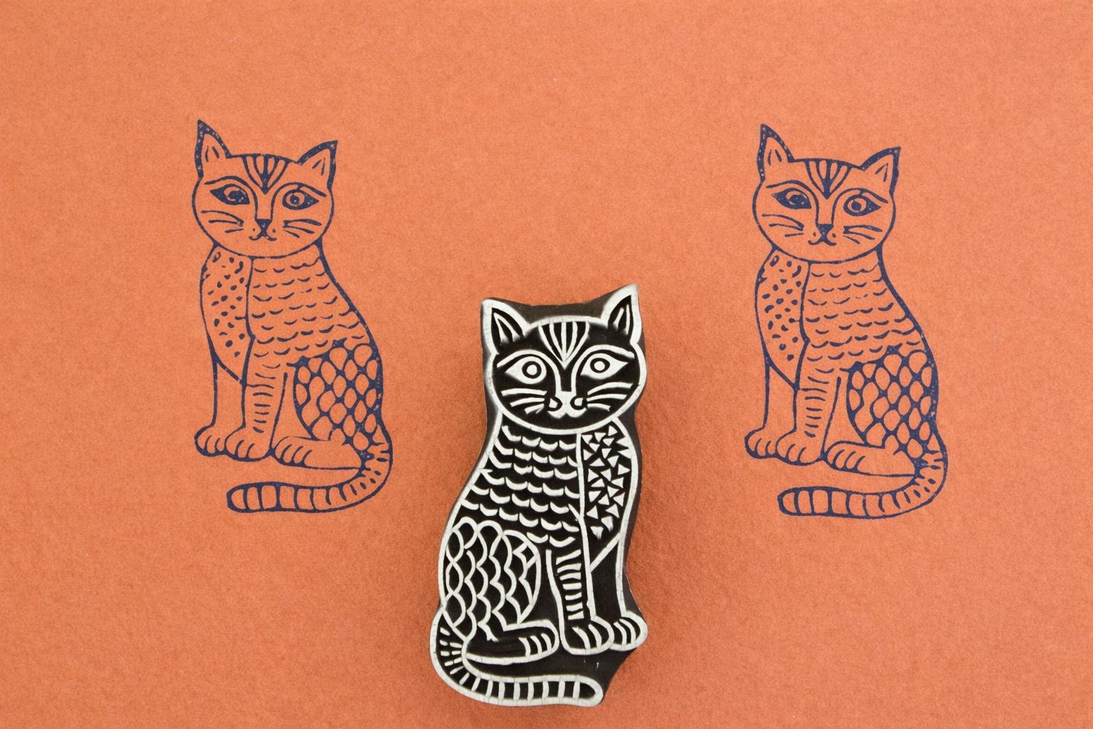 Hand carved wooden stamp of a patterned cat with textured body details printed in dark ink on orange paper