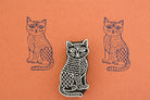 Hand carved wooden stamp of a patterned cat with textured body details printed in dark ink on orange paper