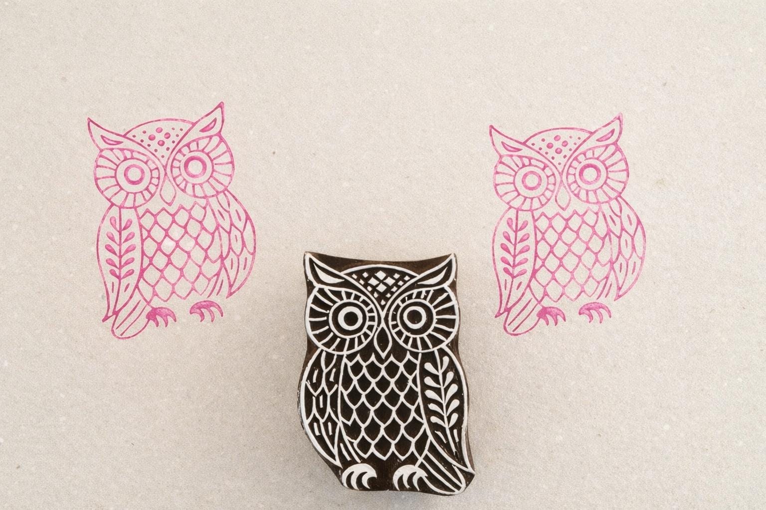 Hand carved wooden owl stamp with feather pattern design printed in pink ink on textured paper