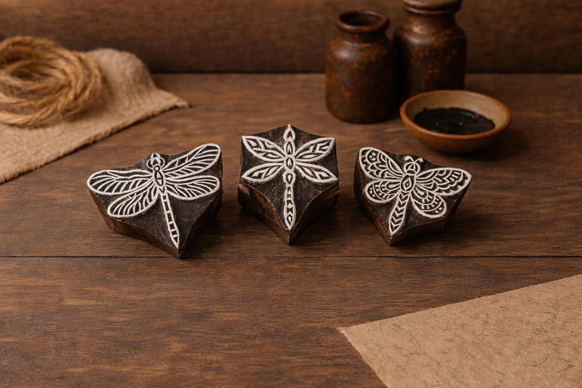 Set of three hand carved wooden block stamps featuring different dragonfly designs on a rustic wooden surface