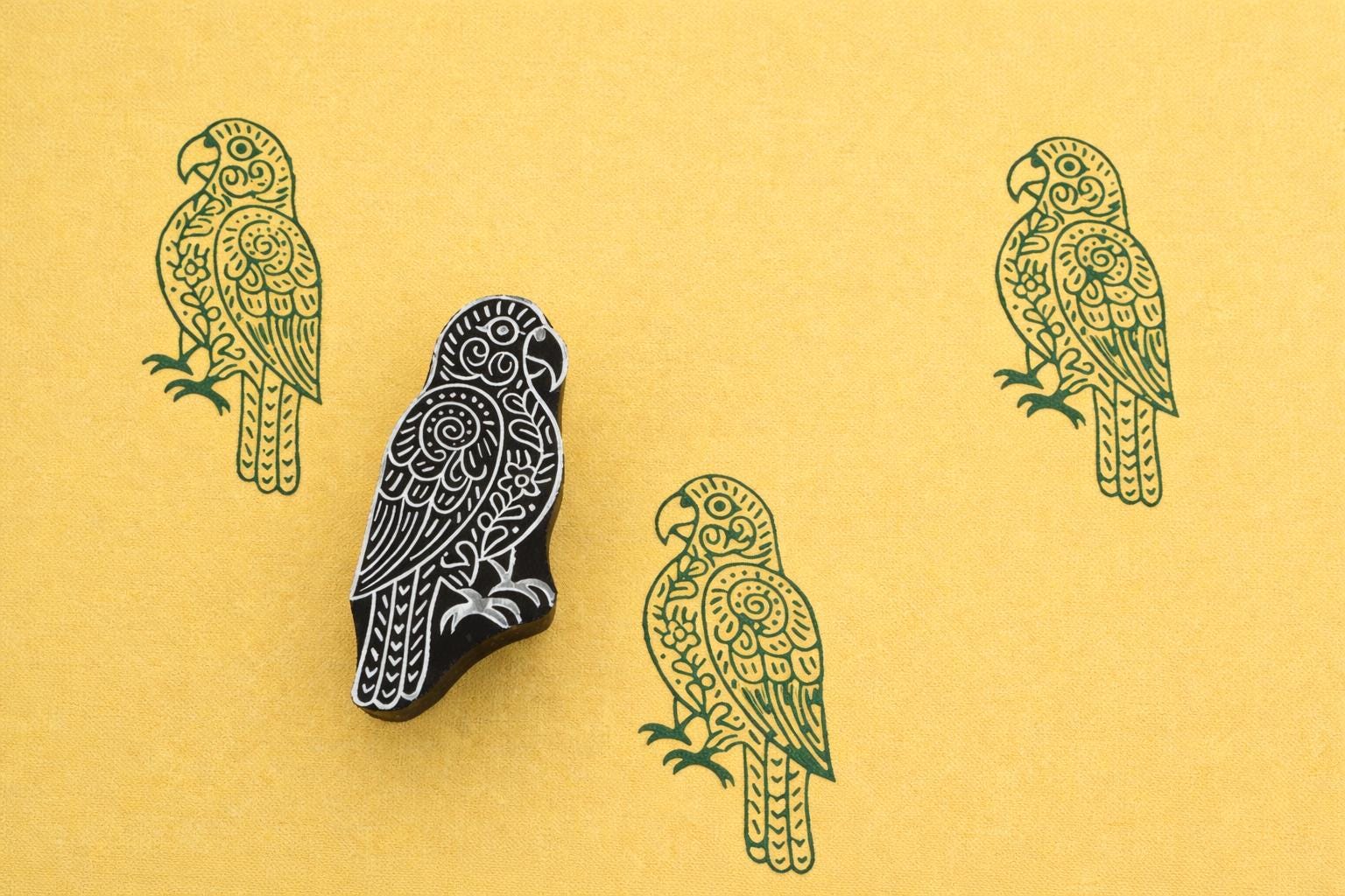 Hand carved wooden block stamp of a decorative parrot with green stamped pattern on yellow paper