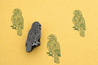 Hand carved wooden block stamp of a decorative parrot with green stamped pattern on yellow paper