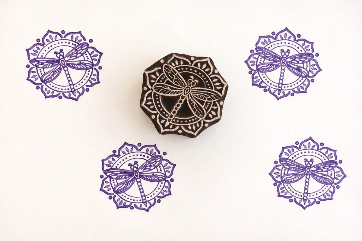 Hand-carved mandala dragonfly stamp with purple prints on paper