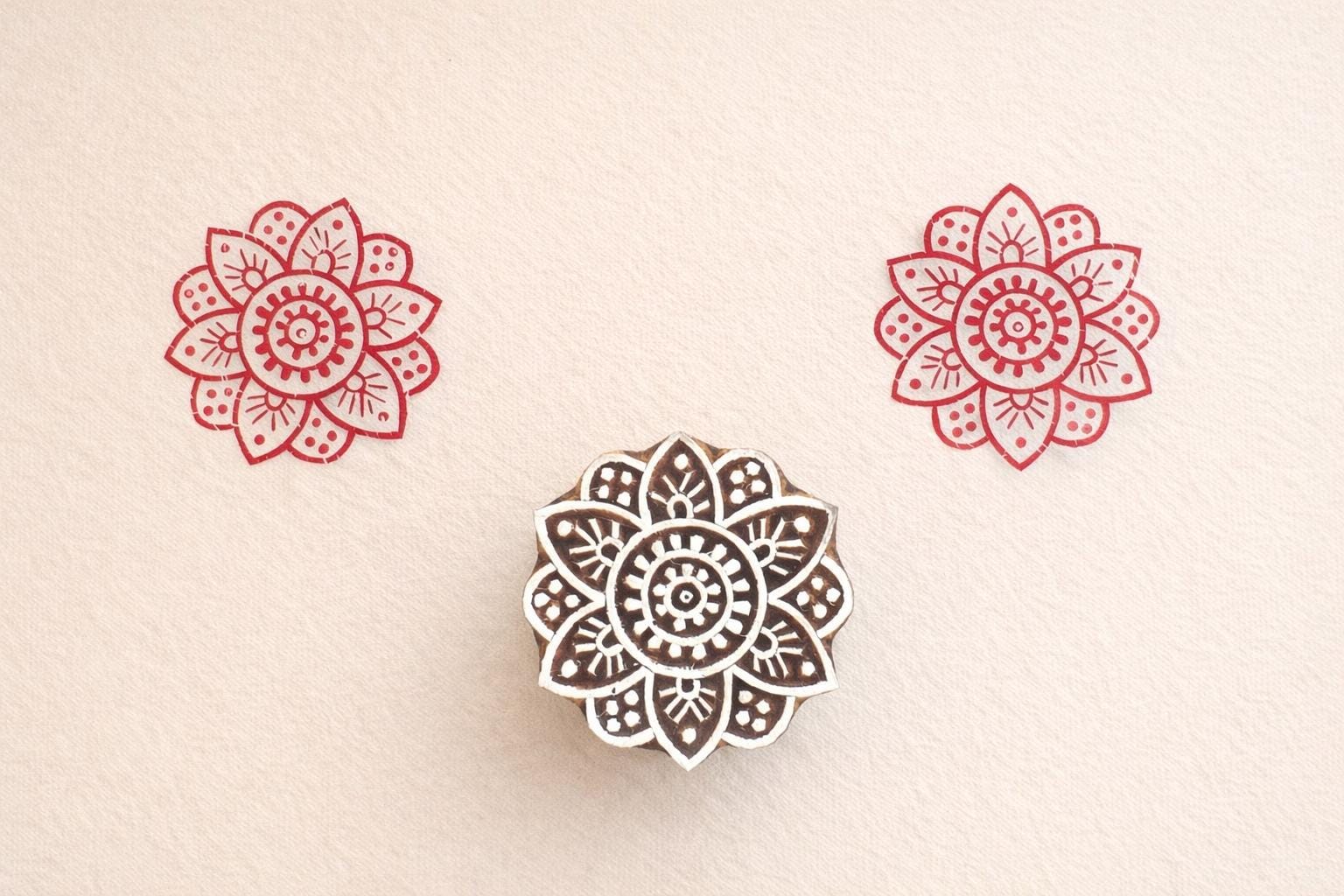 Hand carved wooden stamp printing red floral mandala pattern on fabric
