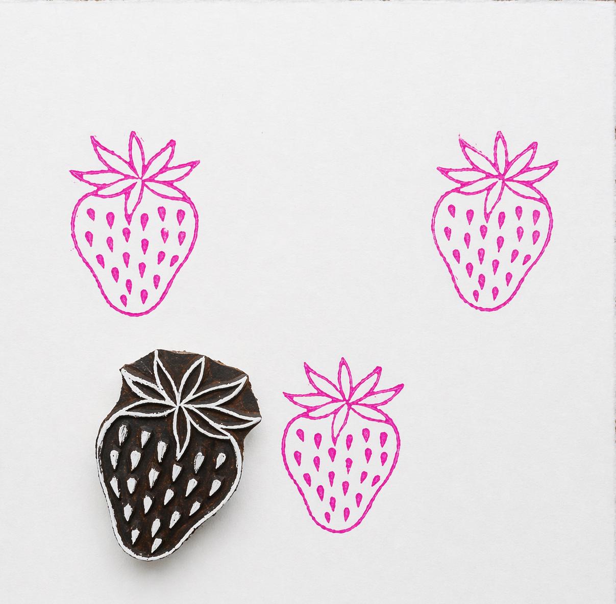 Strawberry wooden printing block creating pink fruit pattern on white background