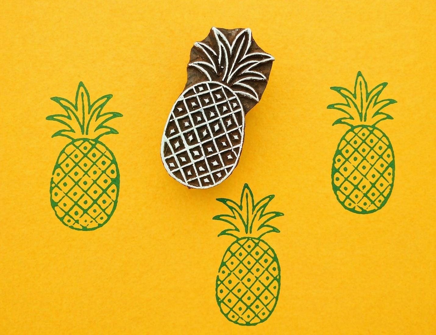 Pineapple wooden printing block creating repeating pattern on yellow fabric background