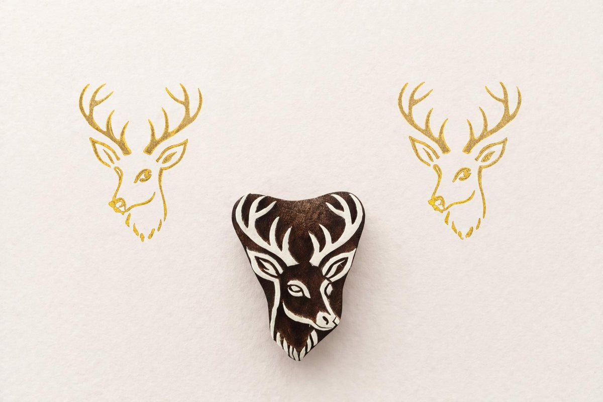 Hand carved wooden deer head stamp with antlers printed in gold ink on textured paper