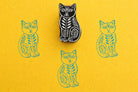 Hand carved wooden stamp of a stylised cat with leaf motifs printed in blue ink on yellow paper