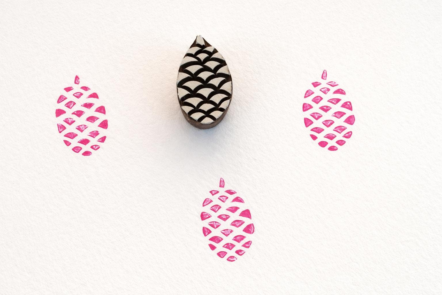 Hand carved wooden pinecone stamp creating repeating pattern prints in pink ink