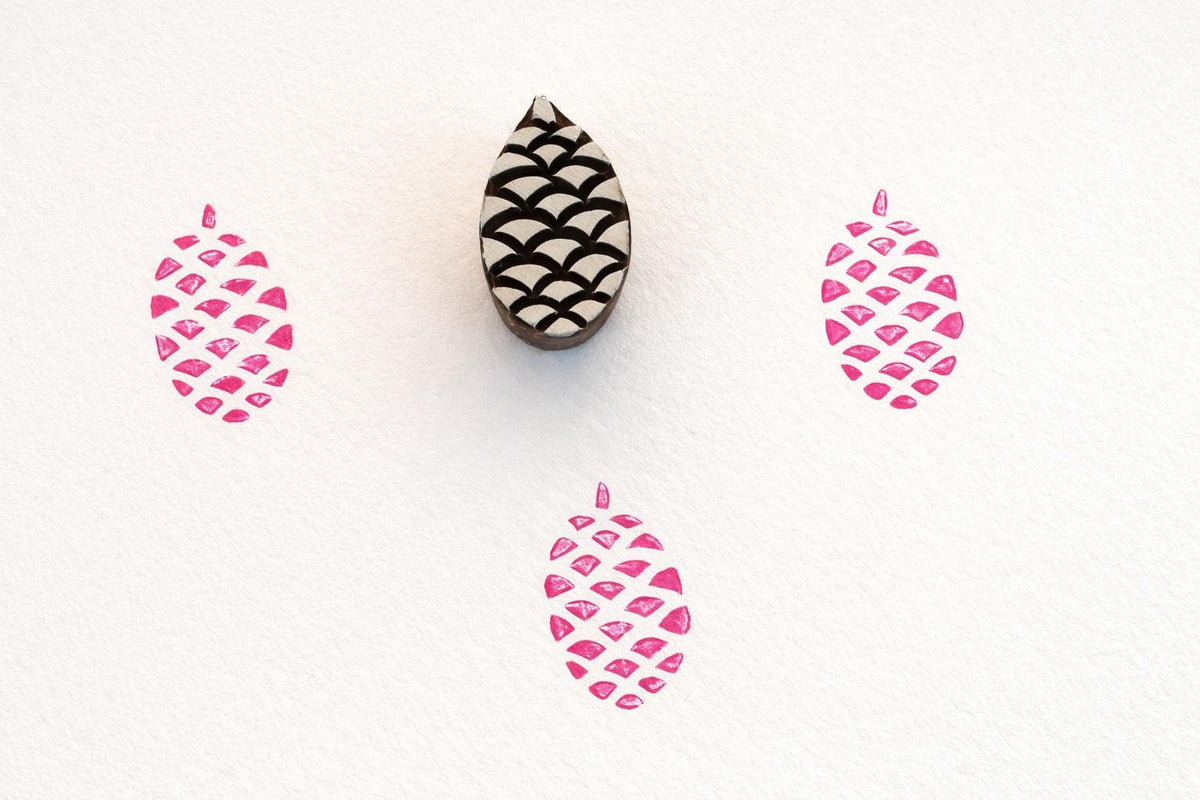 Hand carved wooden pinecone stamp creating repeating pattern prints in pink ink