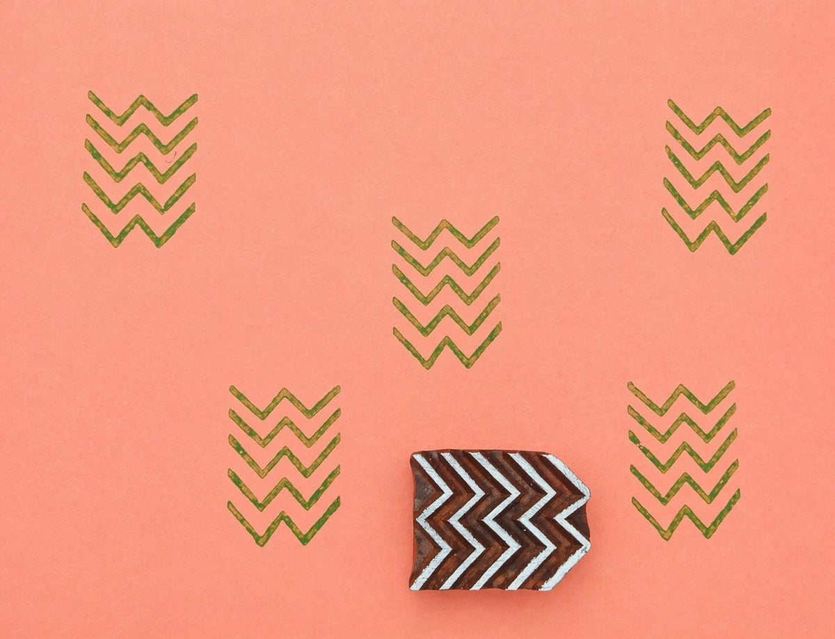 Hand-carved chevron pattern stamp with repeated zigzag print on coral background