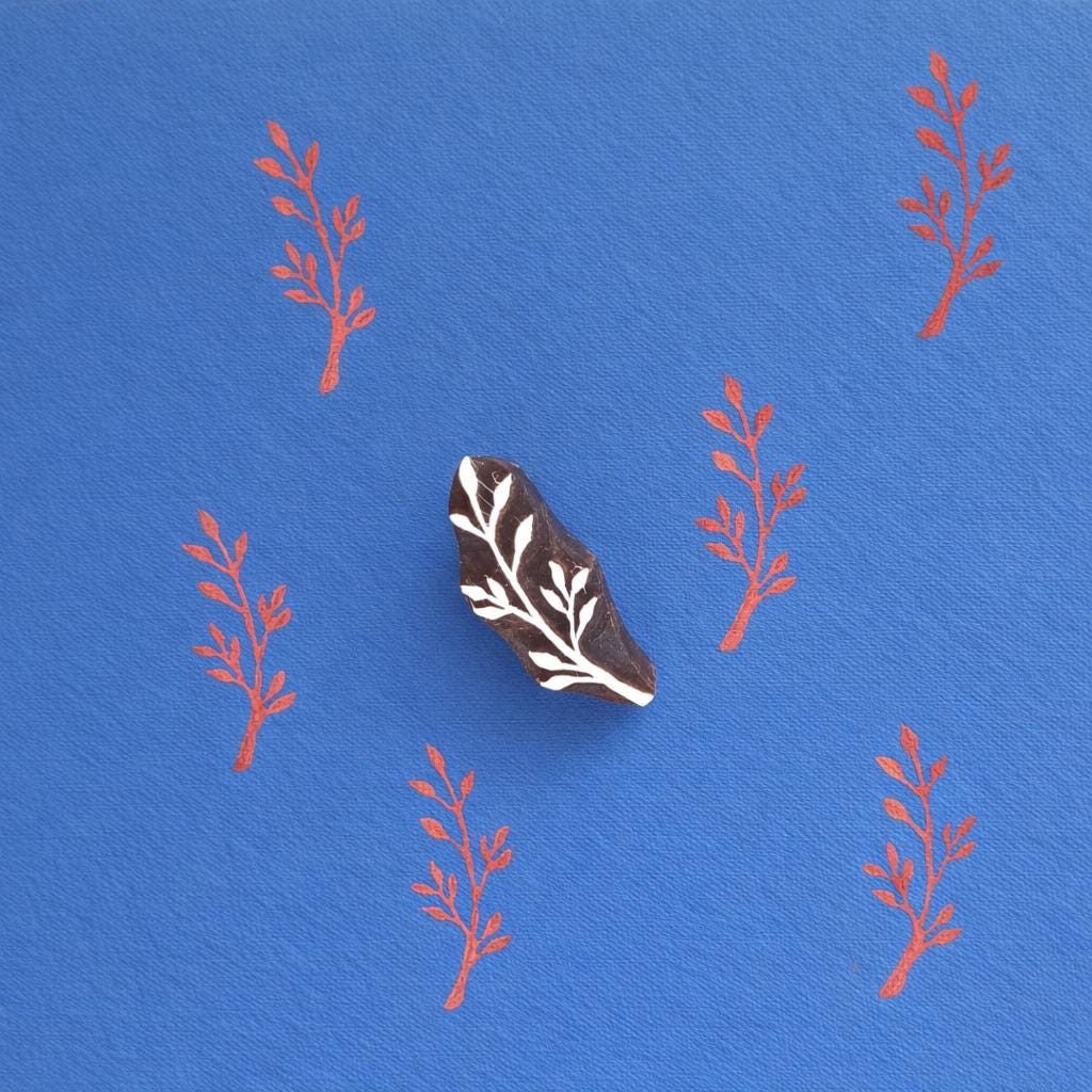 Hand carved twig block printing stamp used to print repeating pattern on blue fabric