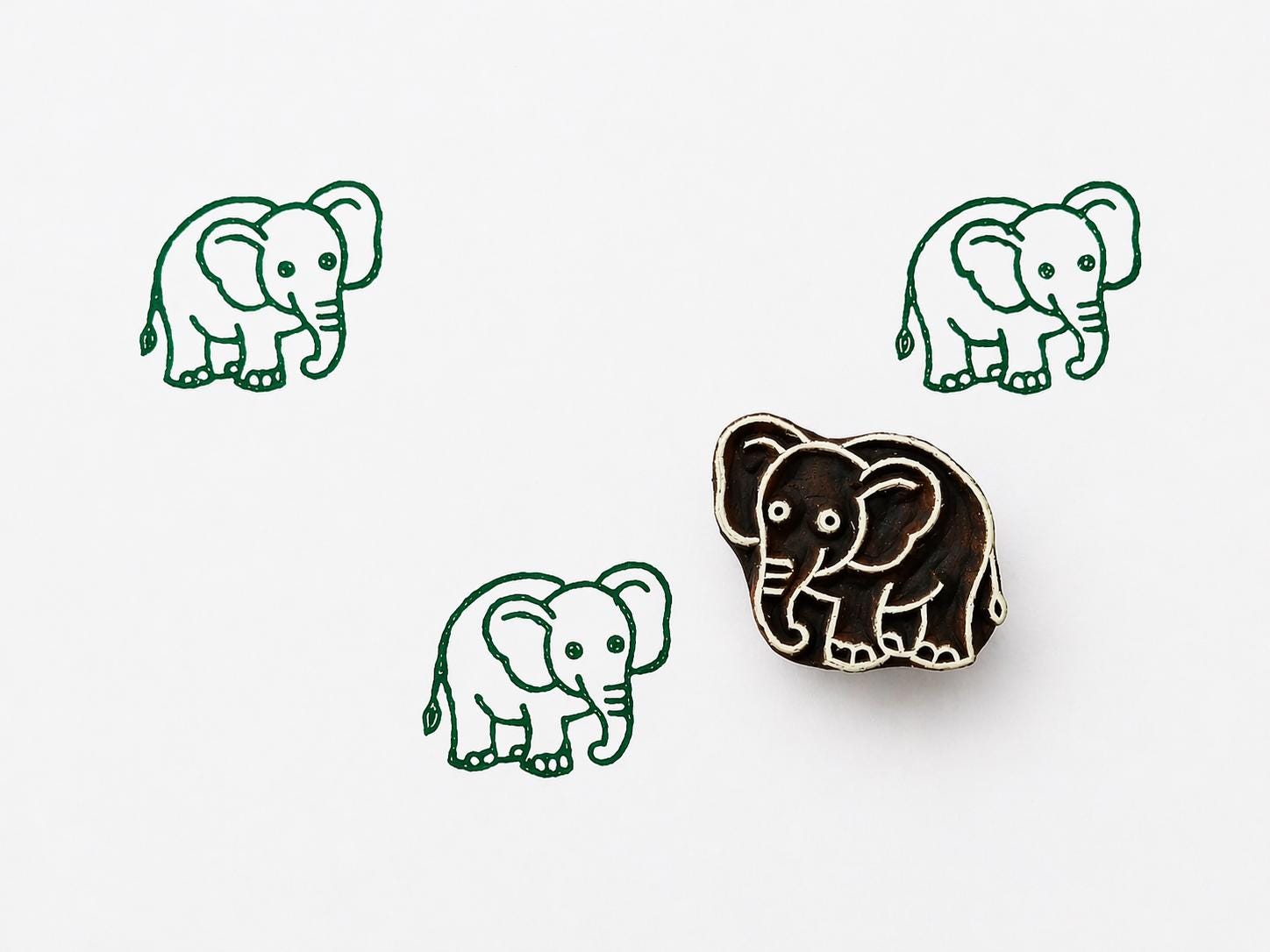 Hand carved wooden elephant printing stamp with repeated green elephant impressions on white background, cute safari animal design for textile printing