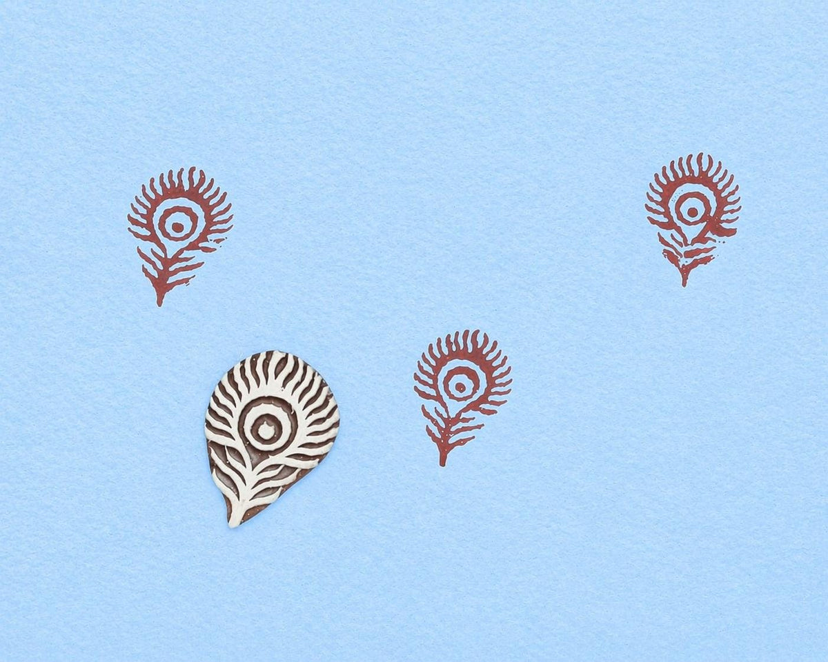 Hand carved wooden block stamp with feather or peacock eye design used for block printing on blue fabric background
