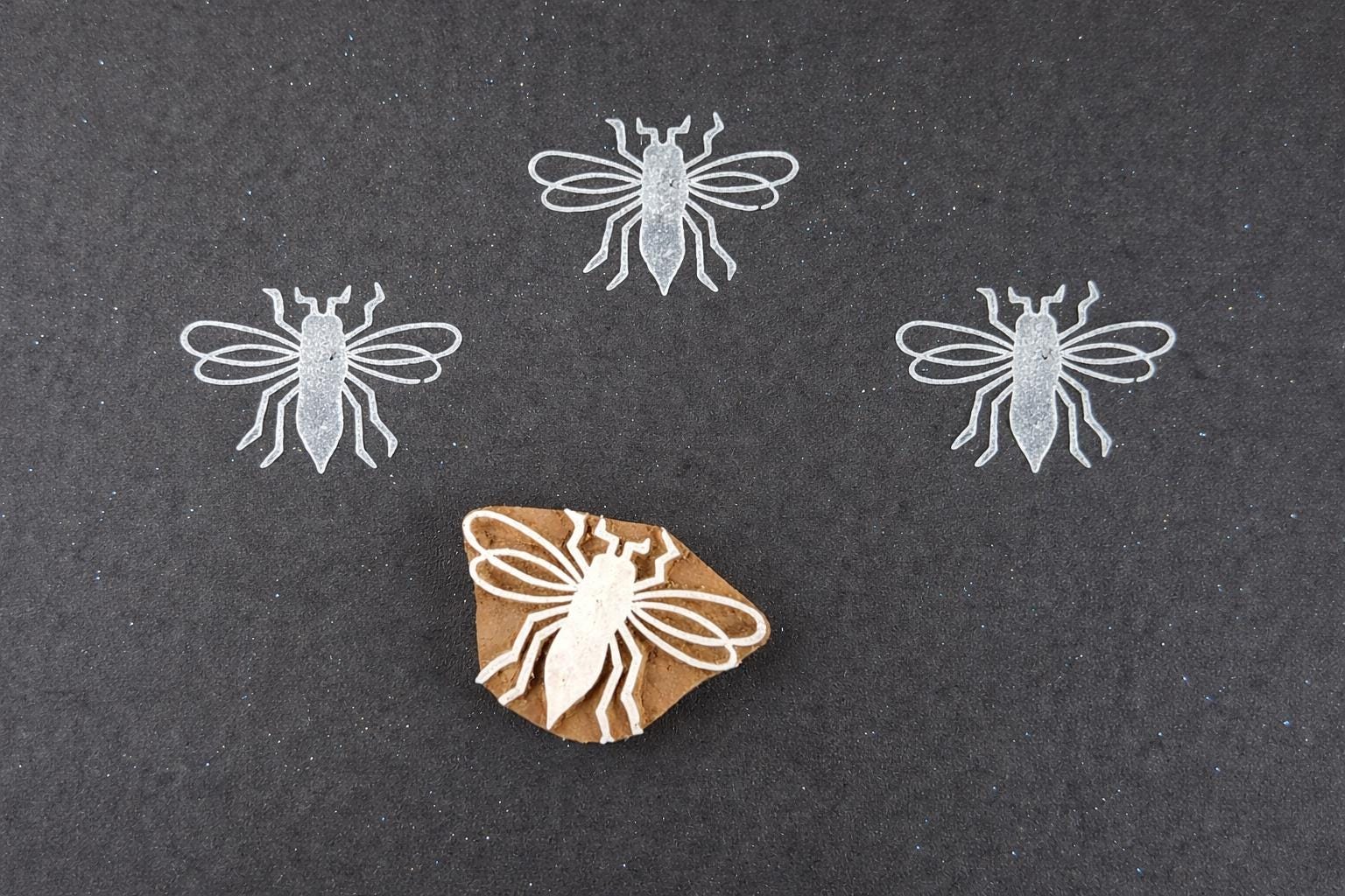 Hand carved wooden block print stamp with bee design creating repeating insect pattern on dark background