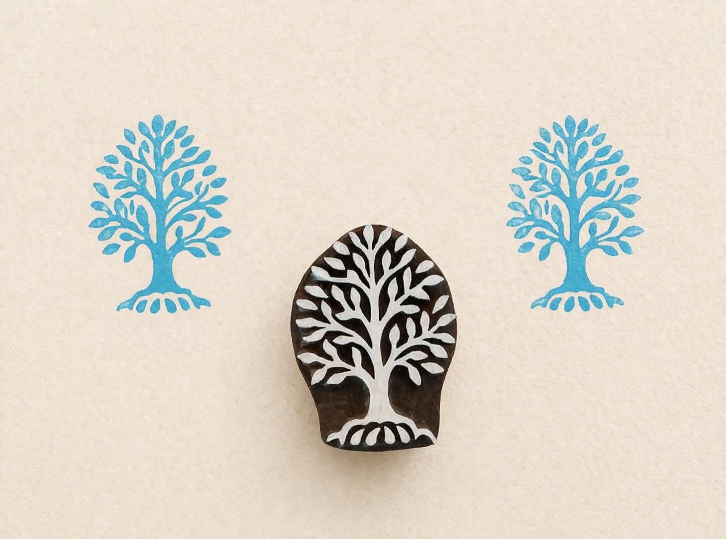 Hand carved wooden stamp with rooted tree design showing visible roots and blue printed impressions on white background
