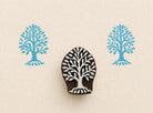 Hand carved wooden stamp with rooted tree design showing visible roots and blue printed impressions on white background
