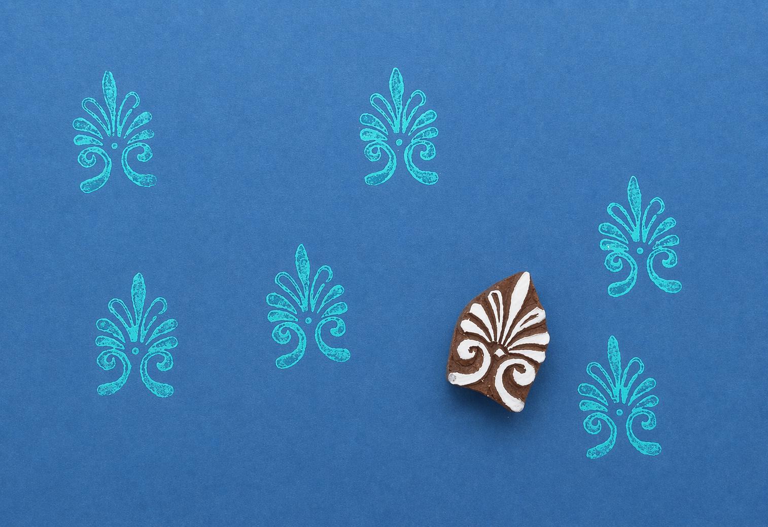 Hand-carved block print stamp with an abstract ornamental pattern repeated on a blue background
