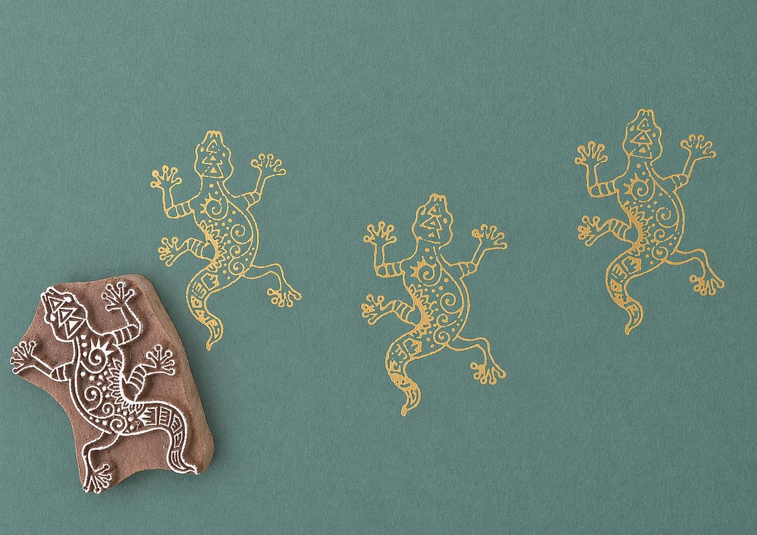Hand carved Indian wooden block printing stamp with lizard design used for fabric, textile, clay, and pottery printing on green background.