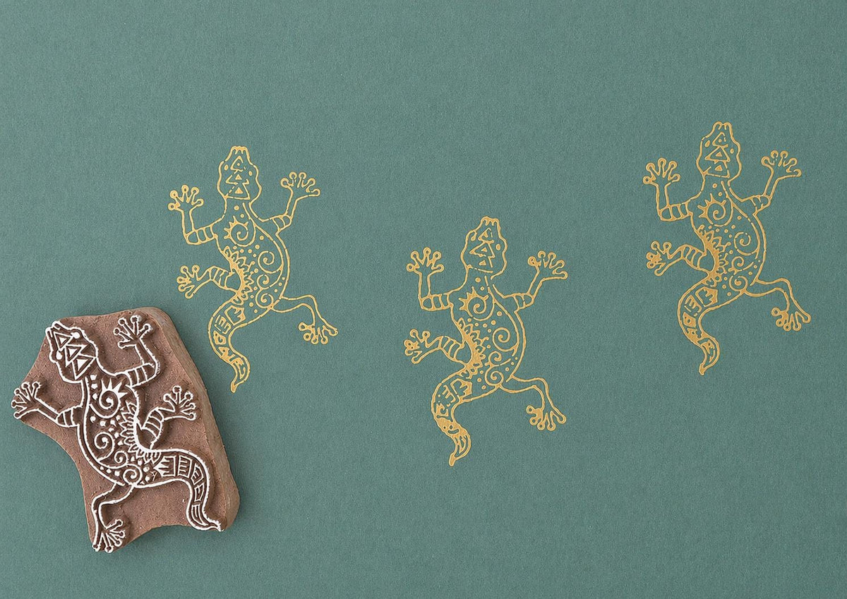 Hand carved Indian wooden block printing stamp with lizard design used for fabric, textile, clay, and pottery printing on green background.