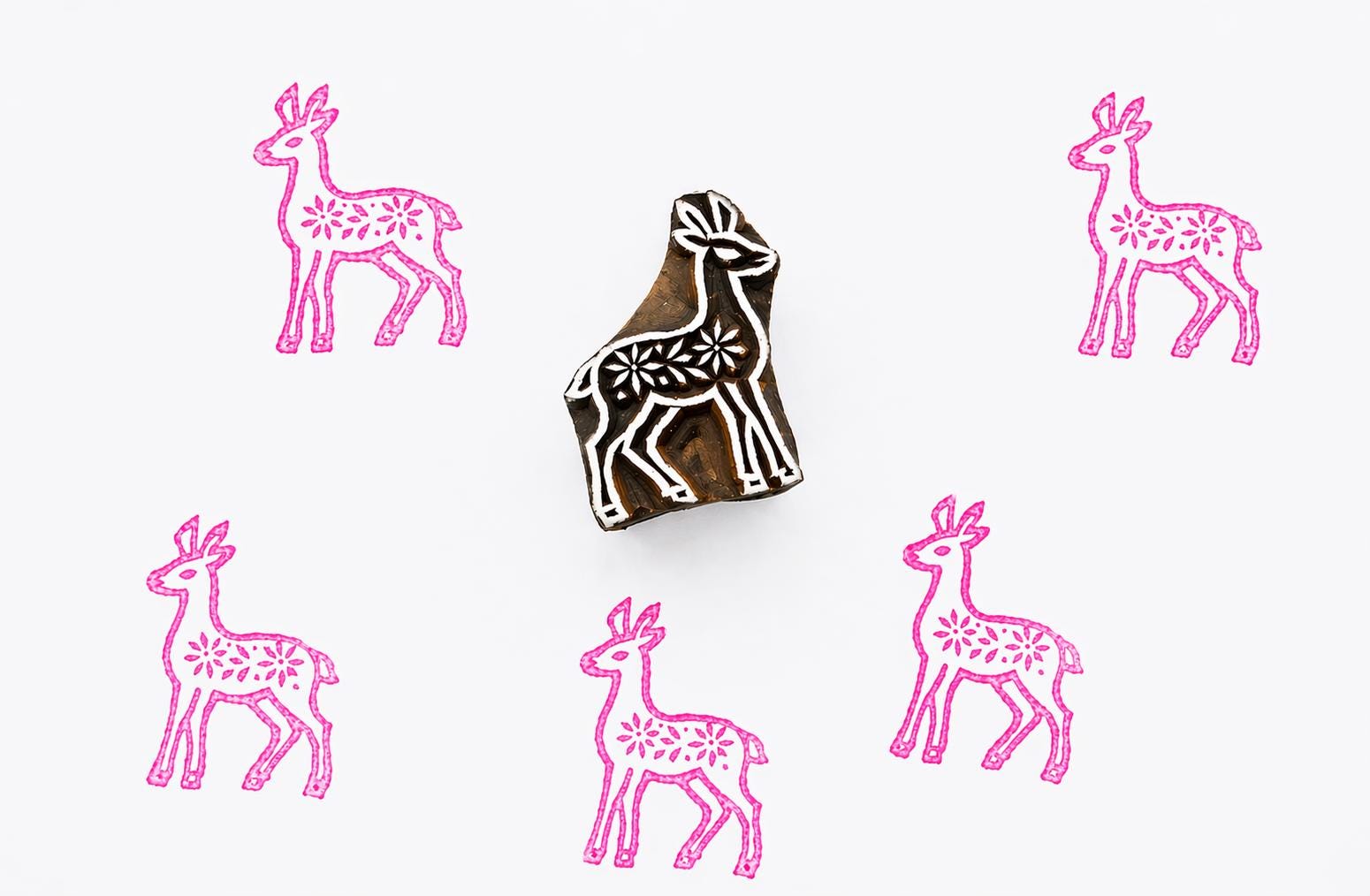 Hand carved wooden block stamp creating a Scandinavian folk style deer pattern with floral details in pink ink